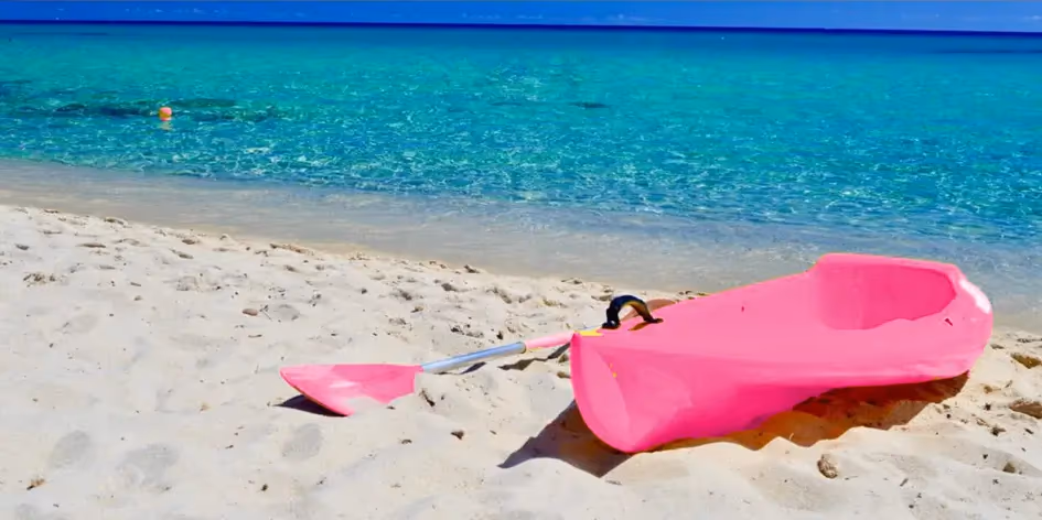 Pinkes Kajak mit Paddel am weissen Sandstrand vor türkisem Meer