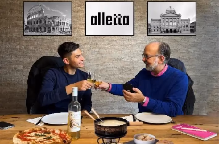 Dy burra ngrenë dolli me fondue dhe pica, në mur fotografia e alletta