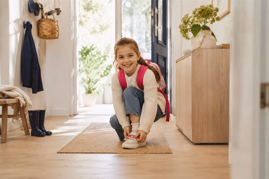 Schulmädchen mit Rucksack zieht im Flur die Schuhe an