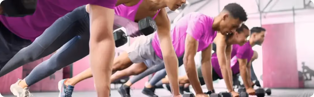 Grupo de t-shirts cor-de-rosa a fazer flexões numa aula de fitness