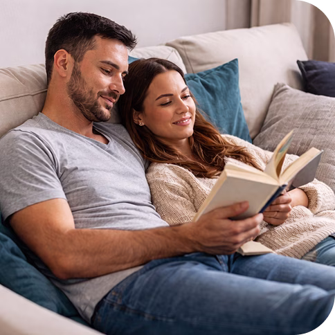 Junges Paar liegt auf Sofa und liest zurfrieden gemeinsam in einem Buch.